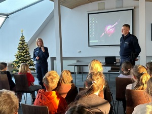 Policjantka i dzielnicowy podczas spotkania z uczniami sępoleńskiej jedynki. Uczniowie siedzą na krzesłach tyłem do zdjęcia. Przed nimi stoi policjantka i policjant.