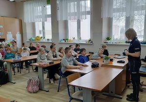 Sala lekcyjna. Policjantka stoi przed uczniami siedzącymi w ławkach szkolnych.
