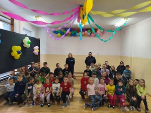 Sala gimnastyczna. Wspólne zdjęcie policjantek z uczniami. Wszyscy zwróceni są twarzą do zdjęcia. Policjantki stoją za uczniami siedzącymi na ławeczkach.