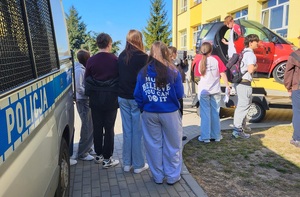 Drzwi otwarte w liceum ogólnokształcącym w Sępólnie Krajeńskim. Uczniowie stoją przy symulatorze dachowania. Dwoje uczniów siedzi w symulatorze, a obok  stoi policjant.