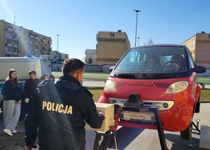 Drzwi otwarte w liceum ogólnokształcącym w Sępólnie Krajeńskim. Uczniowie stoją przy symulatorze dachowania. Dwoje uczniów siedzi w symulatorze, a przed pojazdem stoi policjant obsługujący urządzenie.