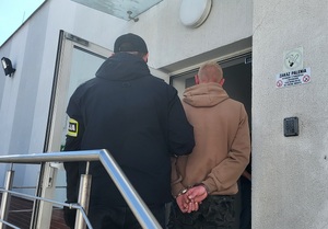 Policjant prowadzi zatrzymanego sprawcę przestępstw