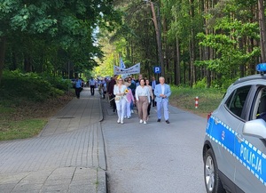 Zdjęcie przedstawia przemarsz uczestników juwenaliów przed którem przemieszcza się policyjny radiowóz