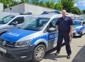 Na zdjęciu mł. asp. Adrian Jędryczka na tle radiowozów policyjnych